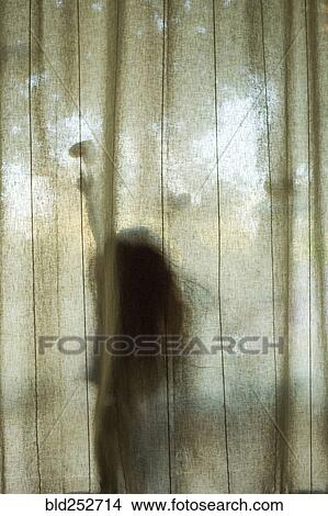 Picture - Silhouette of Caucasian girl touching heart-shape behind window curtain. Fotosearch