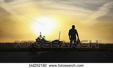 Silhouette of man holding helmet near motorcycle at sunset View Large Photo Image Stock Image - Silhouette of man holding helmet near motorcycle at sunset. Fotosearch