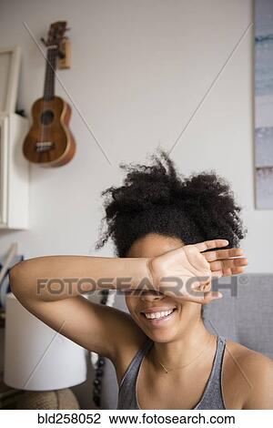 Stock Image - Smiling African American woman covering eyes with arm. Fotosearch