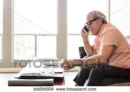 Picture - Smiling and Caucasian man sitting on sofa talking on cell phone. Fotosearch