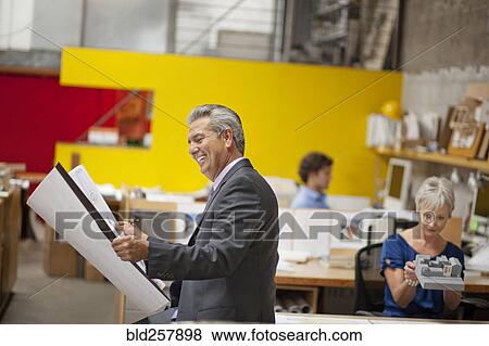 Stock Photo - Smiling architect reading blue1int in office. Fotosearch