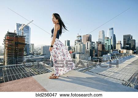 Smiling Asian woman standing on windy urban rooftop View Large Photo Image Stock Photo - Smiling Asian woman standing on windy urban rooftop. Fotosearch