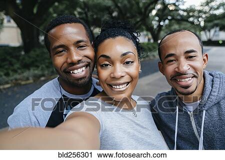 Stock Image - Smiling Black friends posing for cell phone selfie. Fotosearch