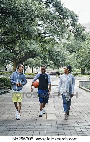Stock Photograph - Smiling Black friends walking in park with basketball. Fotosearch