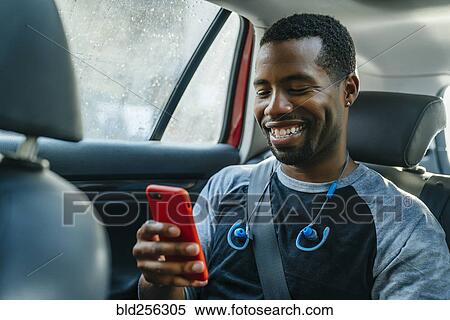 Stock Photography - Smiling Black man texting on cell phone in car. Fotosearch