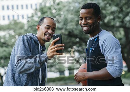 Stock Image - Smiling Black men texting on cell phone. Fotosearch