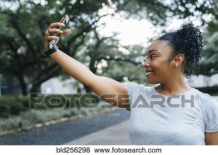 Stock Photo - Smiling Black woman posing for cell phone selfie. Fotosearch