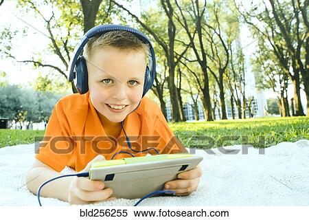 Smiling Caucasian boy laying on blanket in park listening to digital tablet View Large Photo Image Stock Photography - Smiling Caucasian boy laying on blanket in park listening to digital tablet. Fotosearch