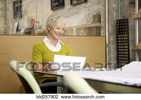 Stock Image - Smiling Caucasian businesswoman reading paperwork in office. Fotosearch