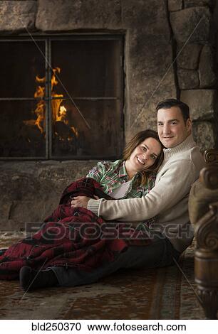 Stock Image - Smiling Caucasian couple cuddling on floor near fireplace. Fotosearch