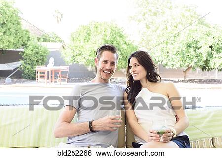 Stock Photograph - Smiling Caucasian couple relaxing with cold drinks outdoors. Fotosearch