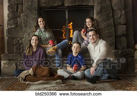 Stock Photograph - Smiling Caucasian family sitting near fireplace. Fotosearch