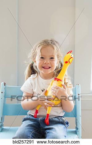 Stock Image - Smiling Caucasian girl holding rubber chicken. Fotosearch
