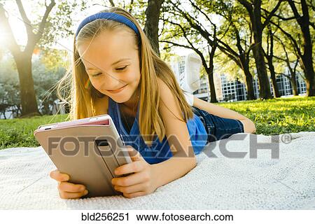 Smiling Caucasian girl laying on blanket in park reading digital tablet View Large Photo Image Stock Image - Smiling Caucasian girl laying on blanket in park reading digital tablet. Fotosearch