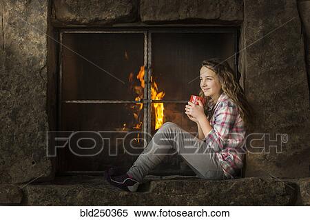 Stock Photography - Smiling Caucasian girl sitting near fireplace. Fotosearch
