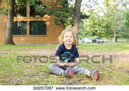 Stock Photo - Smiling Caucasian girl sitting on ground outside house. Fotosearch