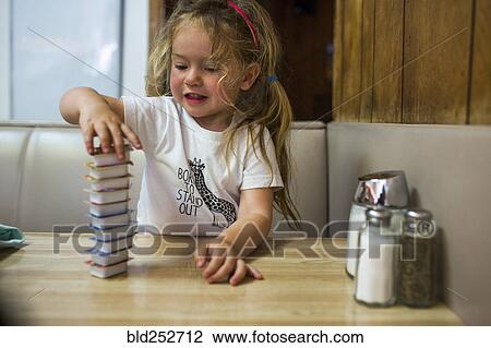 Stock Image - Smiling Caucasian girl stacking jelly containers in restaurant booth. Fotosearch