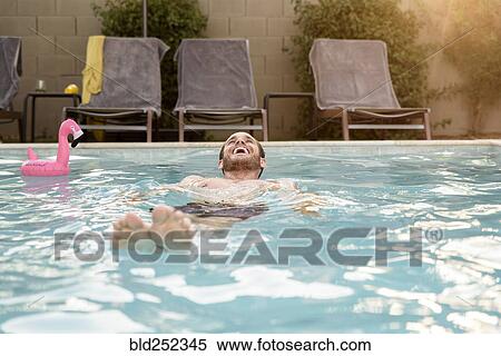 Stock Photography - Smiling Caucasian man floating in swimming pool. Fotosearch