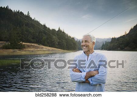 Stock Photo - Smiling Caucasian man standing near lake. Fotosearch