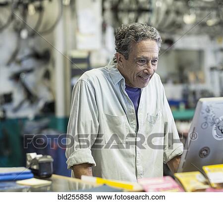 Stock Photo - Smiling Caucasian man using computer in bicycle shop. Fotosearch
