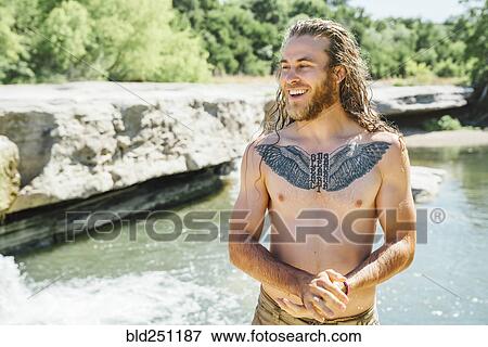 Stock Photo - Smiling Caucasian man with chest tattoo standing near river. Fotosearch