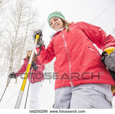 Stock Photo - Smiling Caucasian mother and daughter holding ski poles. Fotosearch