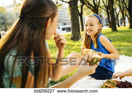 Smiling Caucasian sisters eating food at picnic View Large Photo Image Stock Photo - Smiling Caucasian sisters eating food at picnic. Fotosearch