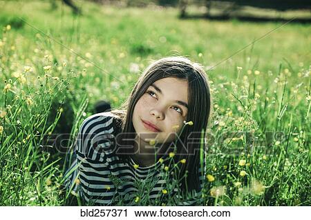 Stock Image - Smiling Caucasian teenage girl laying in grass. Fotosearch
