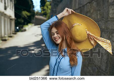 Stock Photograph - Smiling Caucasian woman holding hat near stone wall. Fotosearch