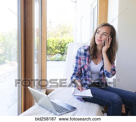 Stock Photo - Smiling Caucasian woman holding paperwork and talking on cell phone. Fotosearch