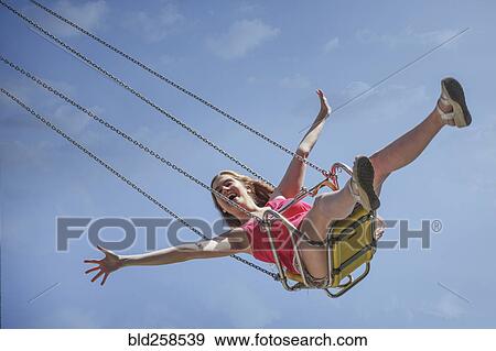Stock Photo - Smiling Caucasian woman riding swing on amusement park ride. Fotosearch