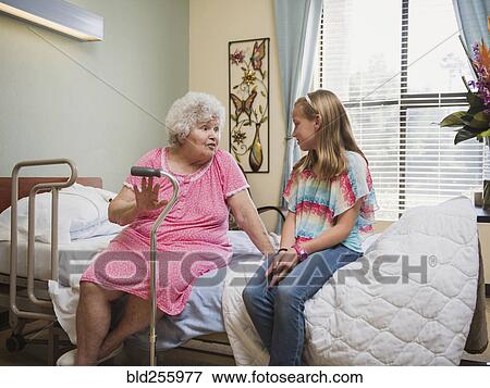 Stock Photo - Smiling Caucasian woman sitting on bed talking to granddaughter. Fotosearch
