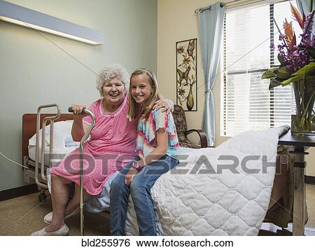 Smiling Caucasian woman sitting on bed with granddaughter View Large Photo Image Stock Photograph - Smiling Caucasian woman sitting on bed with granddaughter. Fotosearch