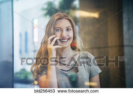 Smiling Caucasian woman talking on cell phone behind window View Large Photo Image Stock Image - Smiling Caucasian woman talking on cell phone behind window. Fotosearch