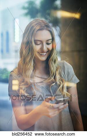 Smiling Caucasian woman texting on cell phone behind window View Large Photo Image Stock Image - Smiling Caucasian woman texting on cell phone behind window. Fotosearch