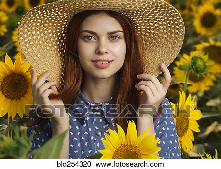 Stock Image - Smiling Caucasian woman wearing hat in field of sunflowers. Fotosearch