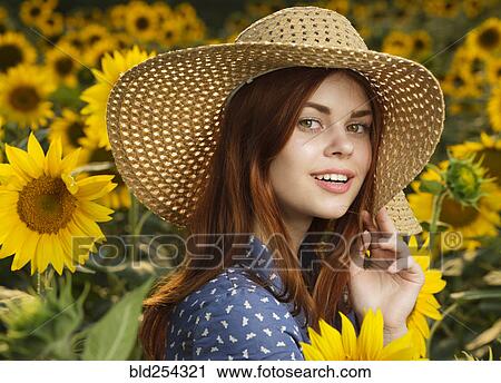 Stock Image - Smiling Caucasian woman wearing hat in field of sunflowers. Fotosearch