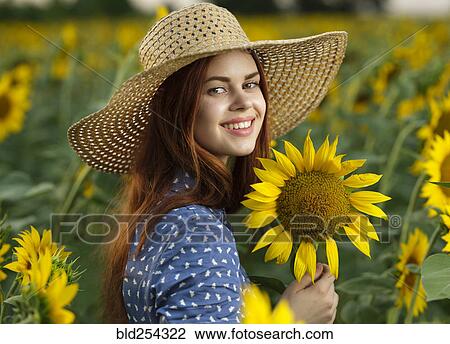 Stock Image - Smiling Caucasian woman wearing hat in field of sunflowers. Fotosearch
