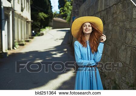 Picture - Smiling Caucasian woman wearing hat near stone wall. Fotosearch