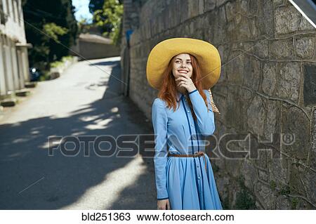 Stock Image - Smiling Caucasian woman wearing hat near stone wall. Fotosearch