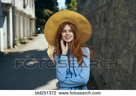Stock Image - Smiling Caucasian woman wearing hat near stone wall. Fotosearch