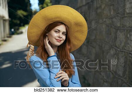 Stock Image - Smiling Caucasian woman wearing hat near stone wall. Fotosearch