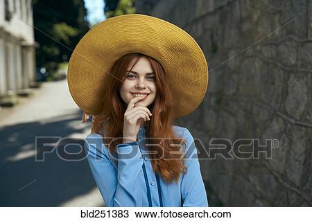 Stock Image - Smiling Caucasian woman wearing hat near stone wall. Fotosearch