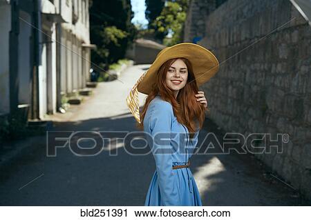Stock Image - Smiling Caucasian woman wearing hat near stone wall. Fotosearch