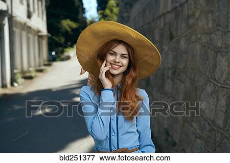 Stock Photo - Smiling Caucasian woman wearing hat near stone wall. Fotosearch