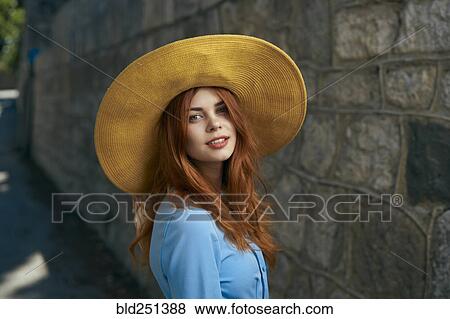 Stock Photo - Smiling Caucasian woman wearing hat near stone wall. Fotosearch