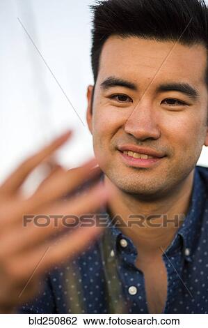 Stock Image - Smiling Chinese man examining grass. Fotosearch