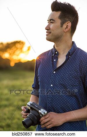Smiling Chinese man holding camera in field View Large Photo Image Stock Photo - Smiling Chinese man holding camera in field. Fotosearch