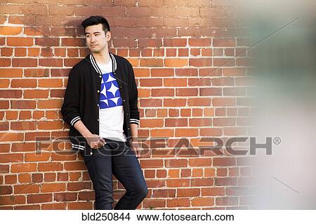 Picture - Smiling Chinese man leaning on red brick wall. Fotosearch