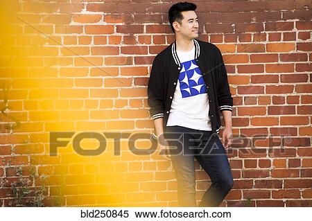 Stock Photography - Smiling Chinese man leaning on red brick wall. Fotosearch